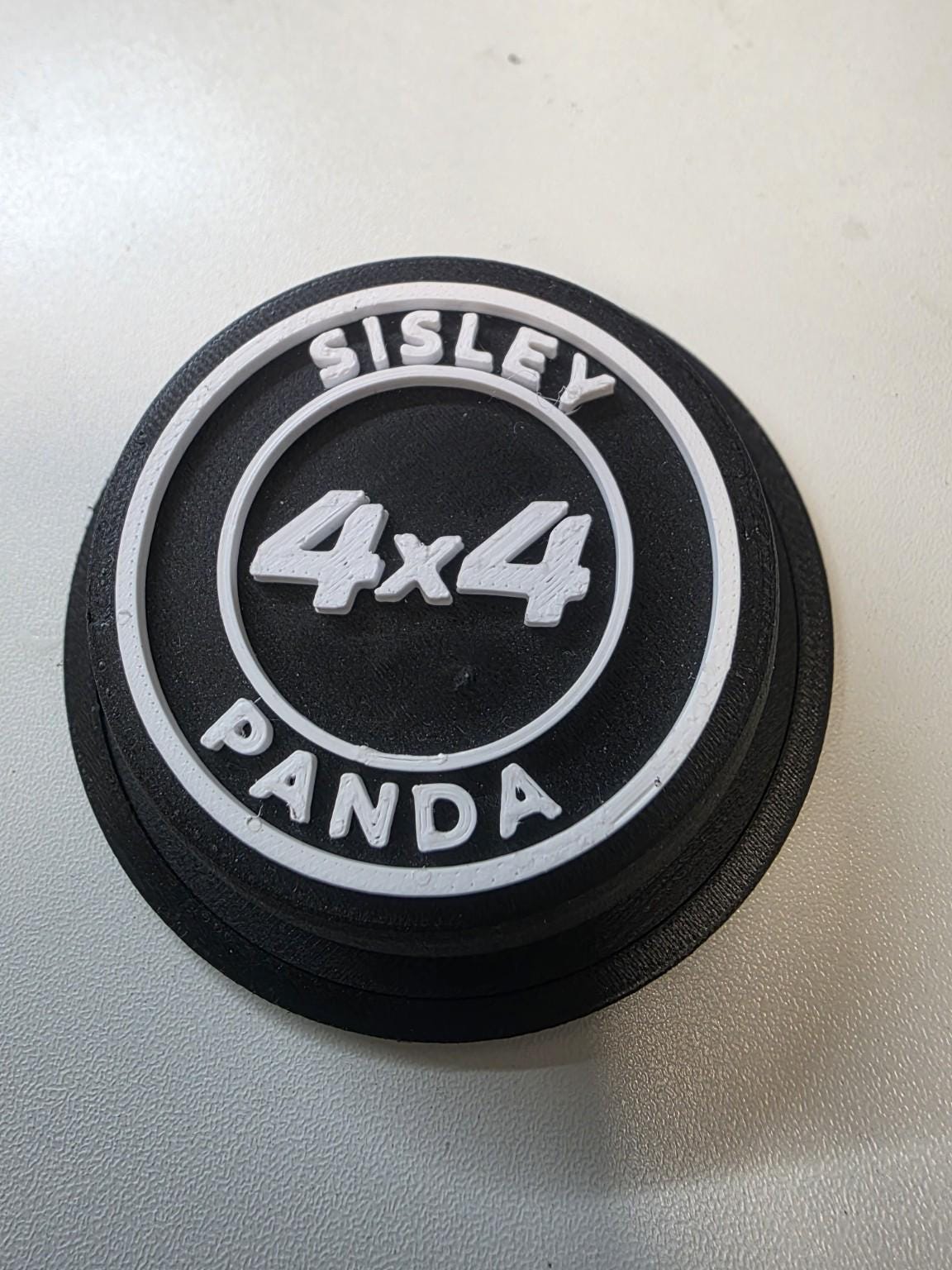 Coprimozzo nero per Fiat Panda 4x4 Sisley in PETG-CF con scritte bianche in rilievo, vista obliqua