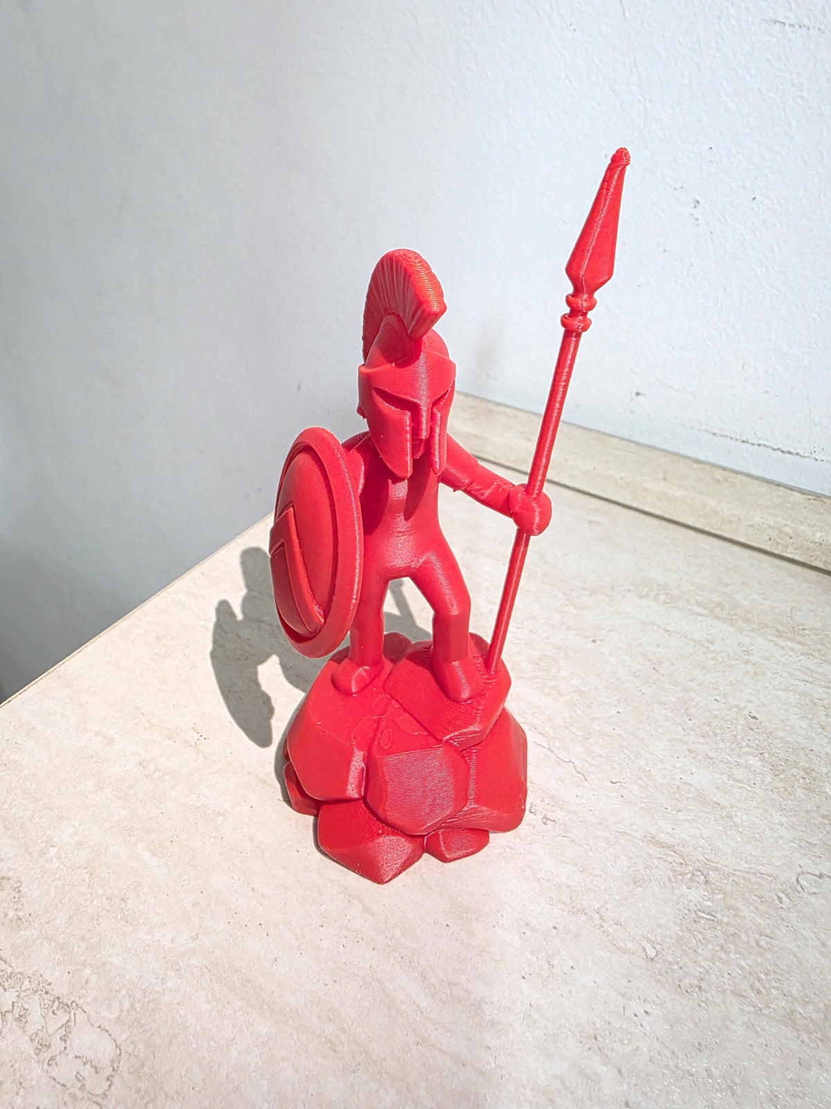 Spartano Fantasy Stick Warrior rosso con elmo, lancia e scudo su base rocciosa