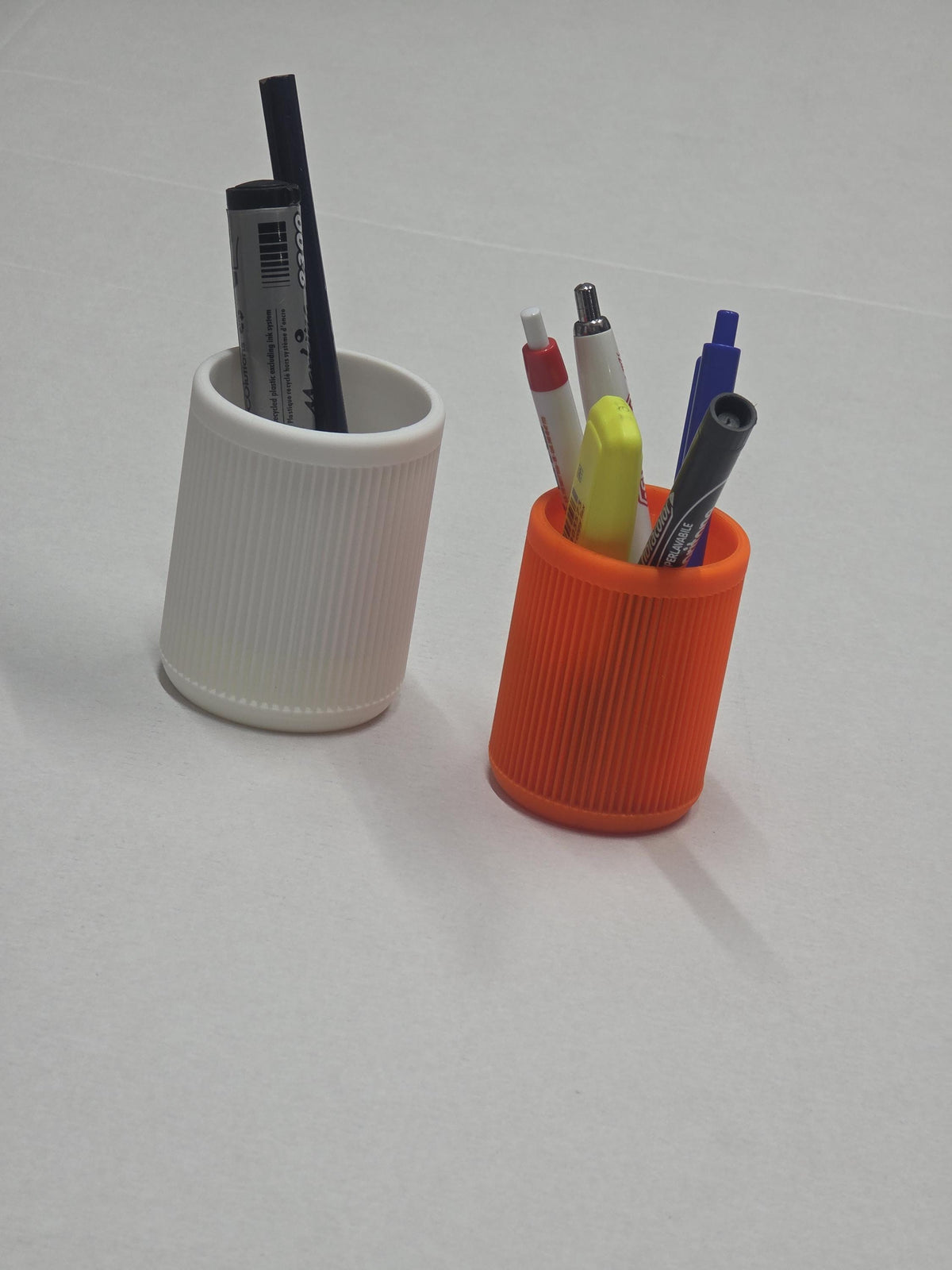 Portapenne rigati in due formati, uno chiaro e uno arancione, con penne e accessori da scrivania