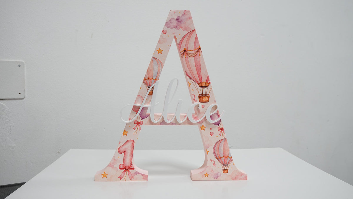 Lettera A da appoggio con nome Alice in rilievo, stampa UV con mongolfiere rosa e numero 1.