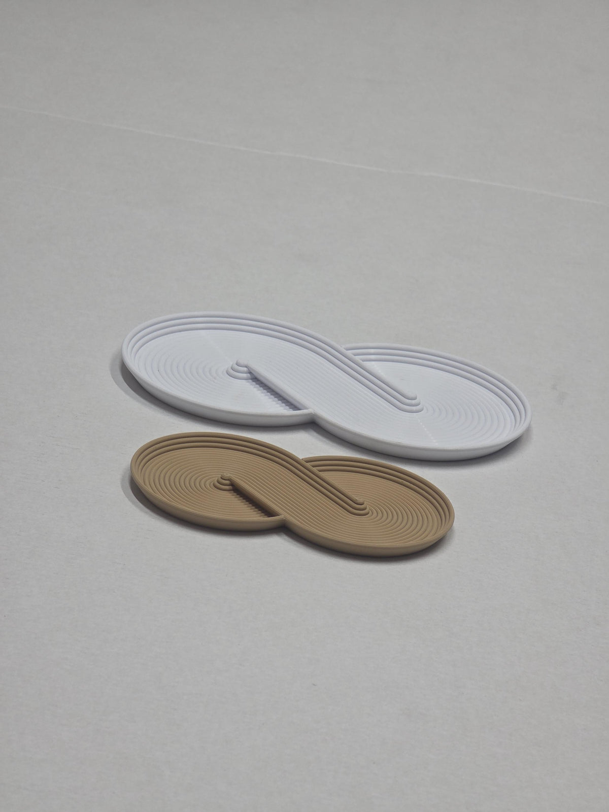 Confronto di due svuotatasche Infinity a forma di infinito, uno chiaro grande e uno beige compatto